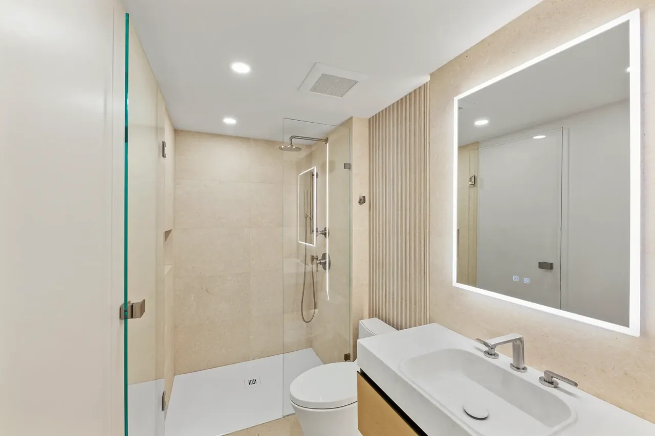 Finished modern bathroom with glass shower, custom vanity, and illuminated mirror