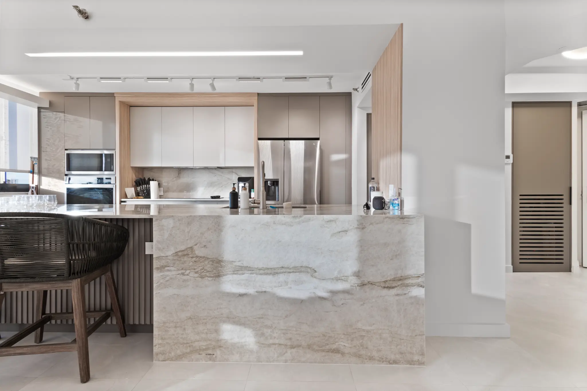 Bright finished kitchen with a stone waterfall island, warm wood detailing, and contemporary cabinetry